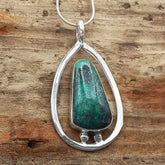 Teardrop-shaped pendant with green Chrysocolla stone and silver frame on a wooden background